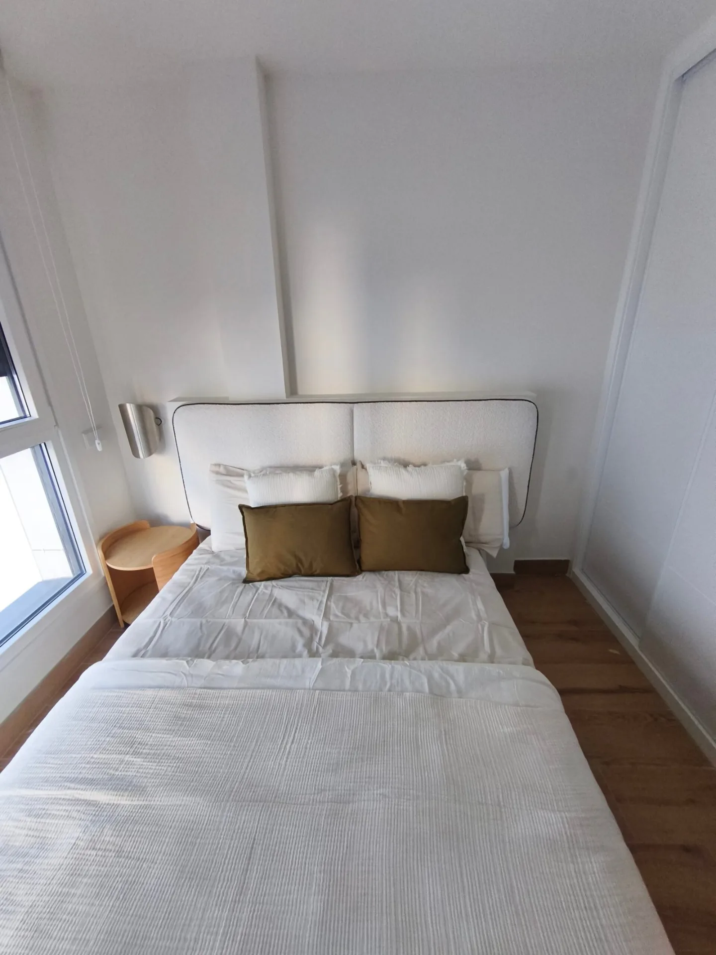 Cama de matrimonio con cabecero blanco y cojines en un dormitorio