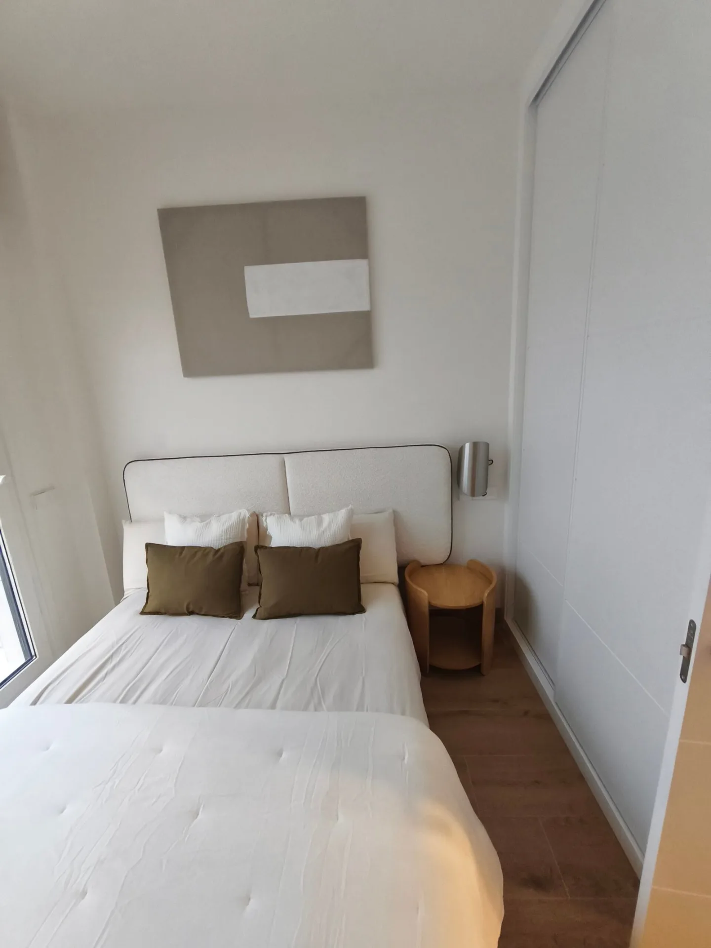 Cama de matrimonio con cabecero blanco y cojines en un piso amueblado