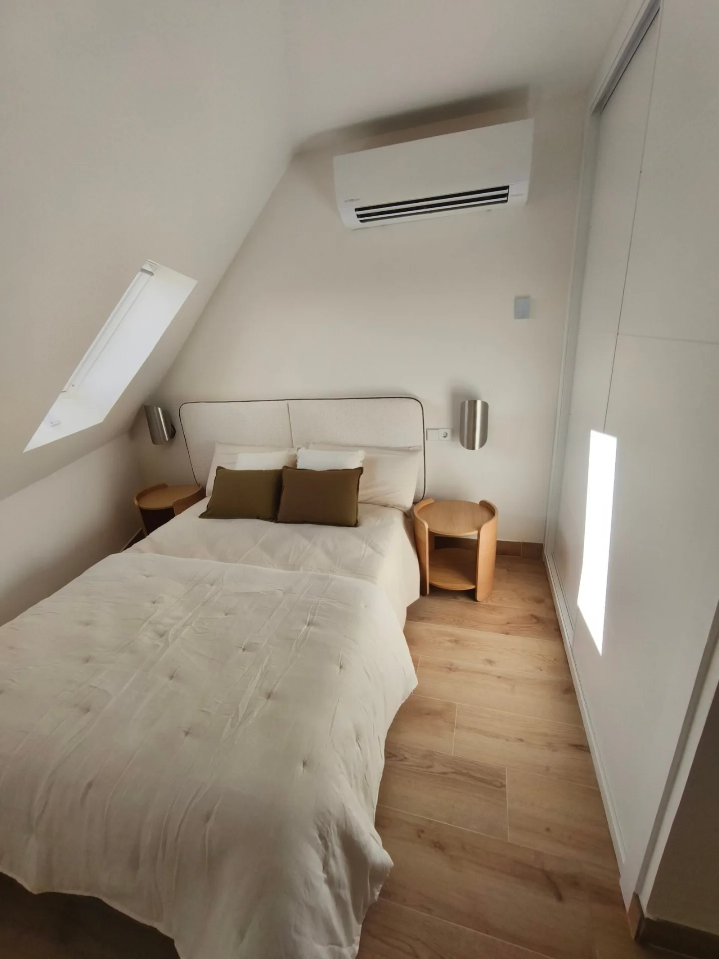Dormitorio abuhardillado con cama de matrimonio, aire acondicionado y mesitas de noche en un piso amueblado