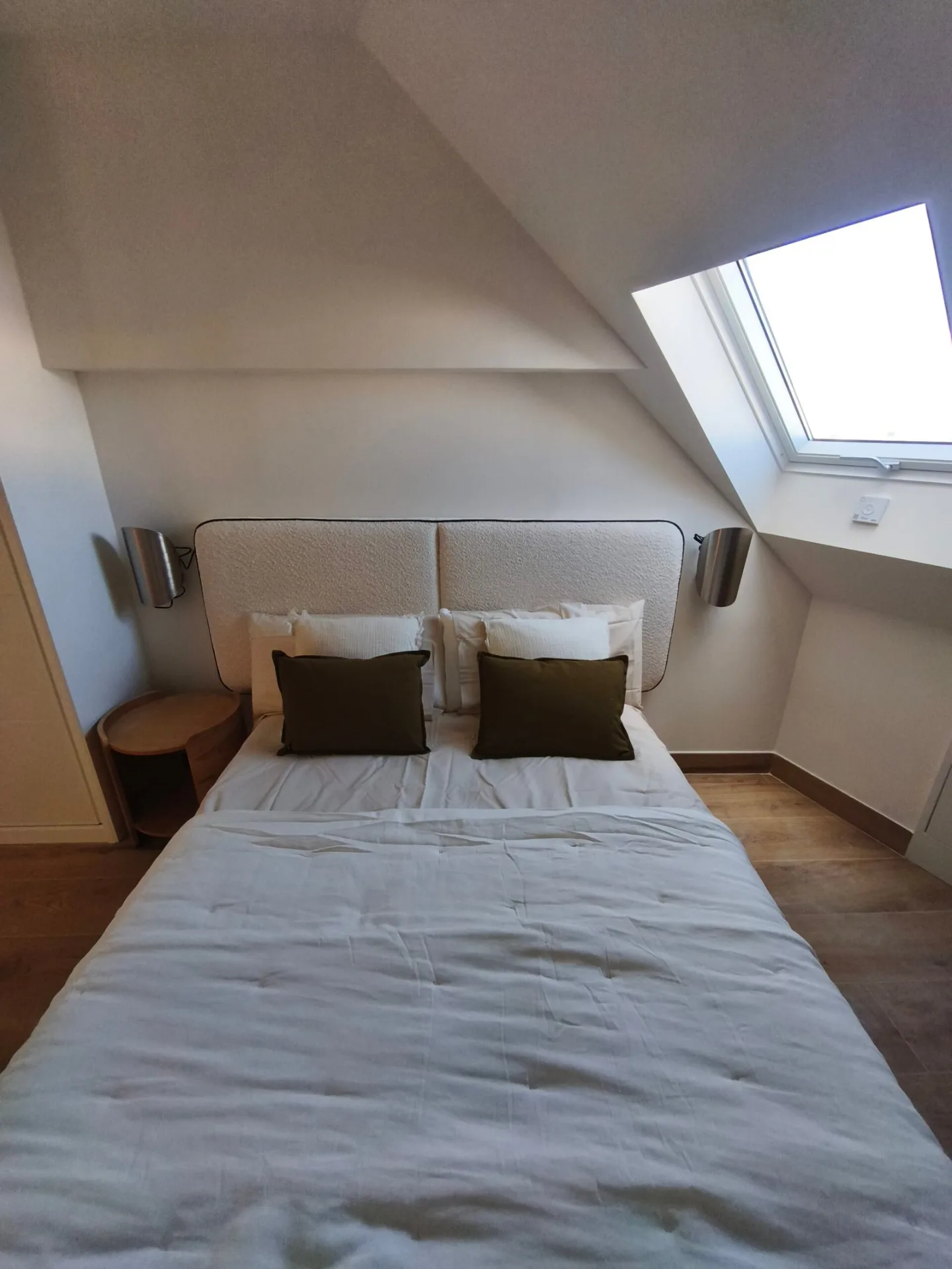 Dormitorio abuhardillado con cama de matrimonio, mesitas de noche y ventana de techo