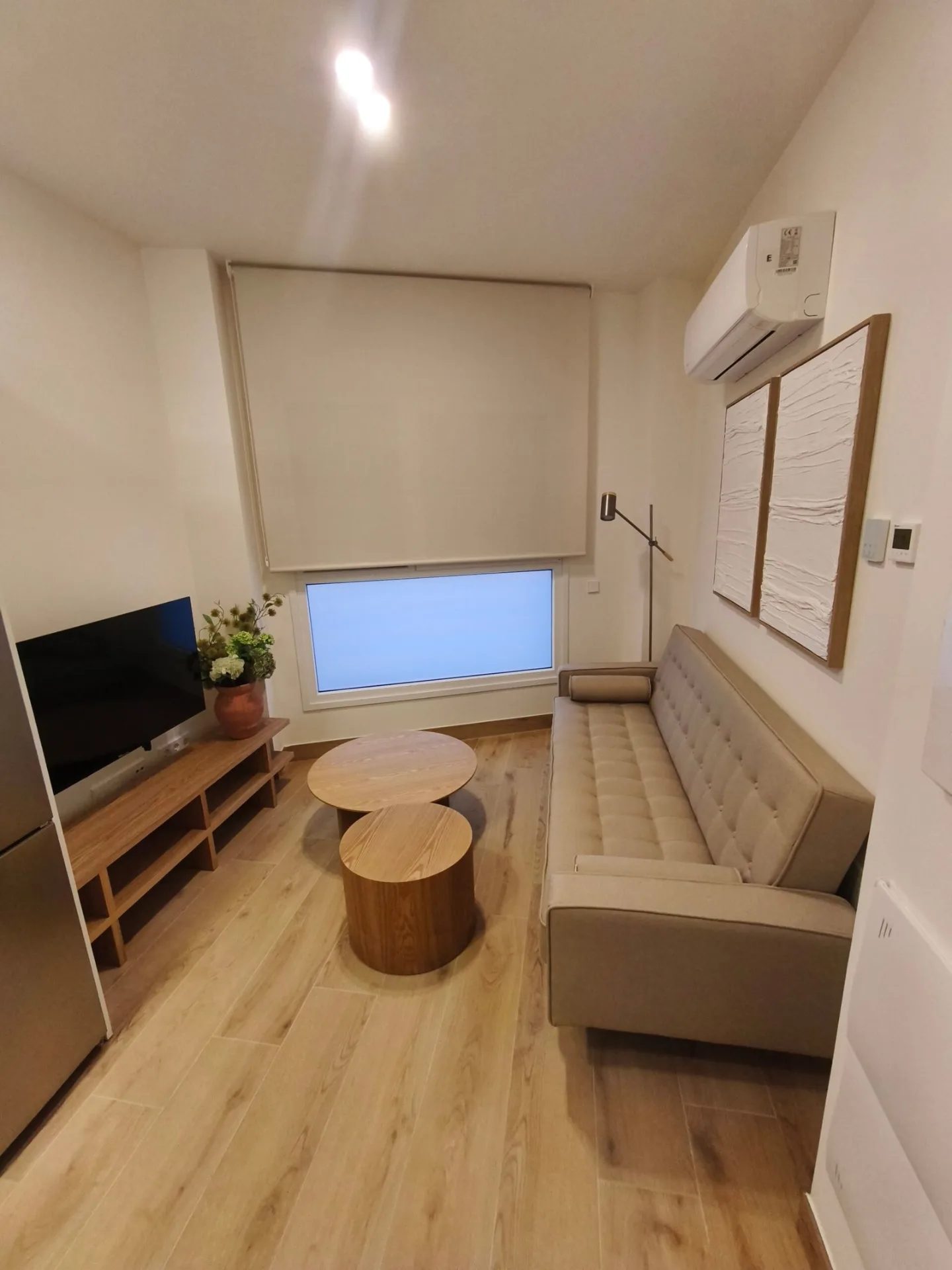 Salón con sofá, mueble de TV y mesa de centro redonda de madera en un piso de alquiler